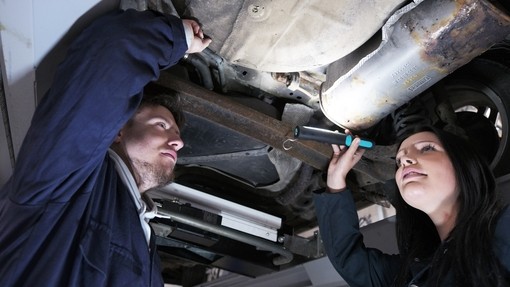 Two students in overalls standing underneath a car and inspecting the mechanics.