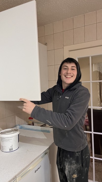 Theo reaching into a cupboard smiling at the camera