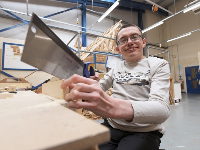 a boy sitting down in a workshop holding a hand saw