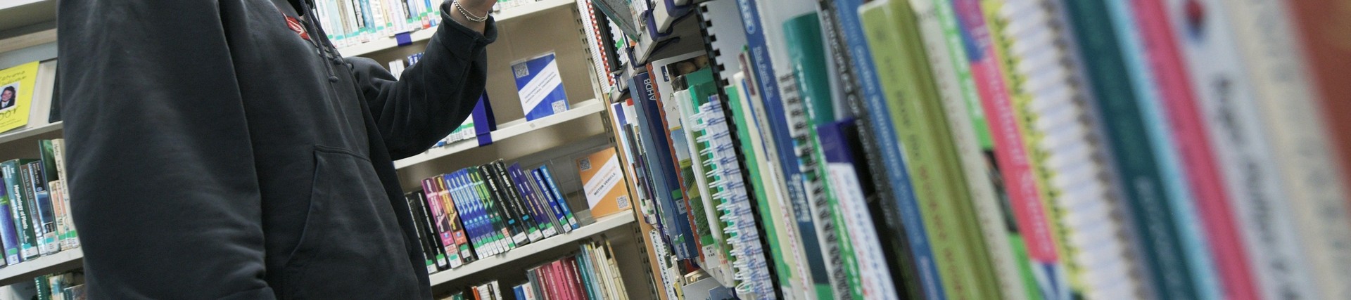 Female student choosing a book from a library shelf.