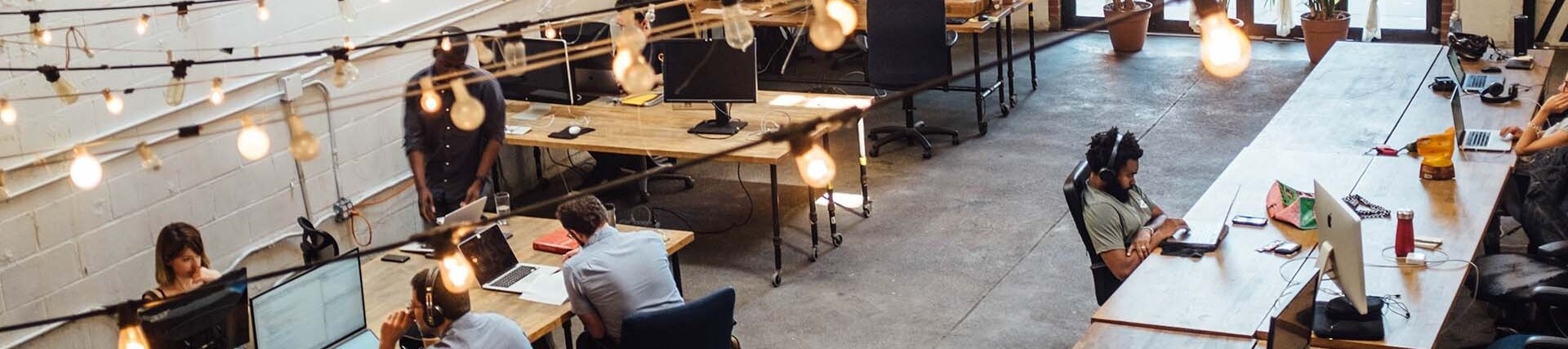 office space with workers sitting at various desk, light dangle from the ceiling