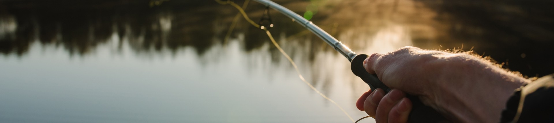 A fishing rod being cast into a lake, the water is calm and the sun is shining in the background