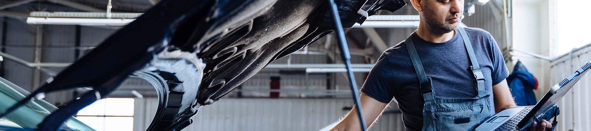 A male is running diagnostics testing on a car engine, the bonnet is open