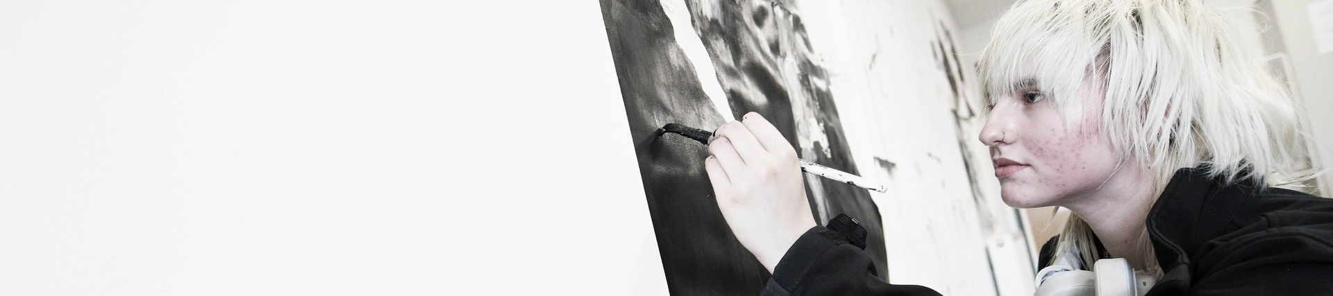 Student white bleached white hair painting on a large canvass with black paint