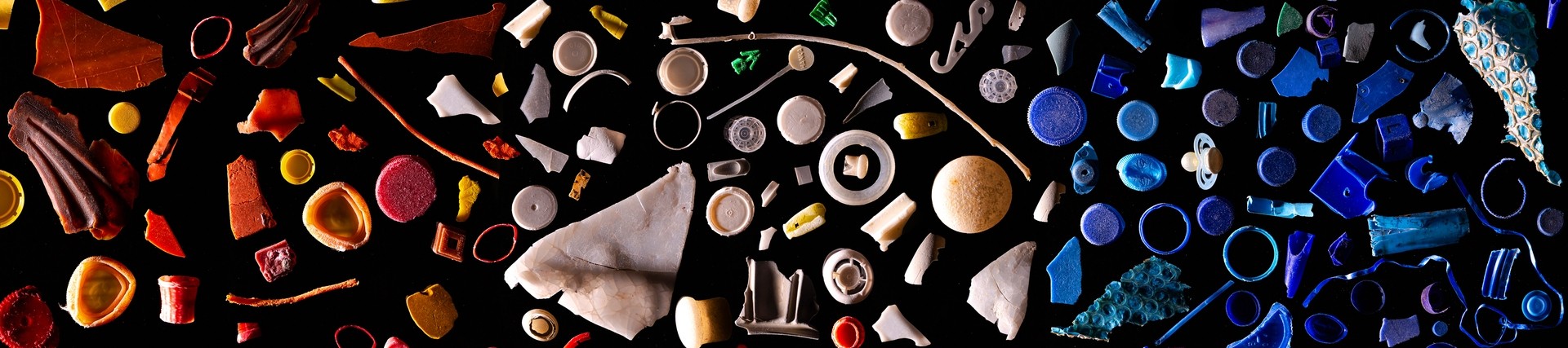 close up image of lots of pieces of micro plastics, arranged by colour on a black background, like a mosaic