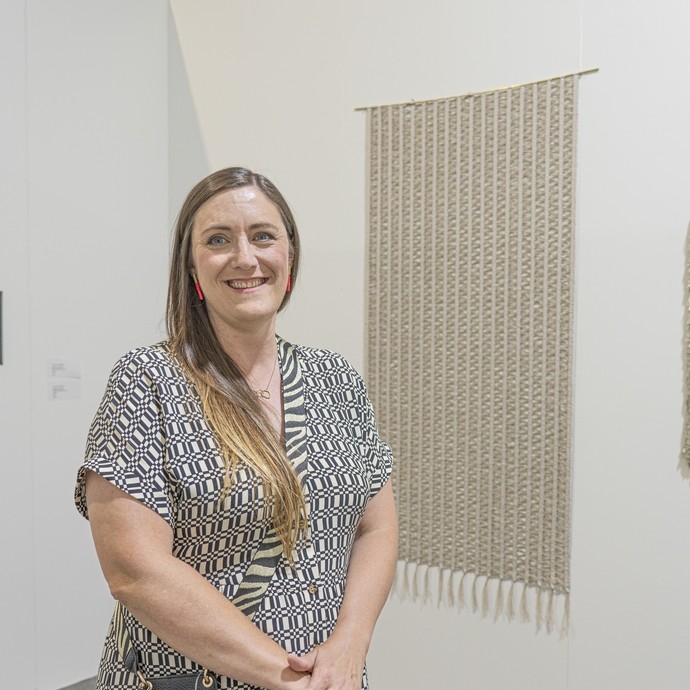 Laura Thomas stood in gallery in front of her artwork