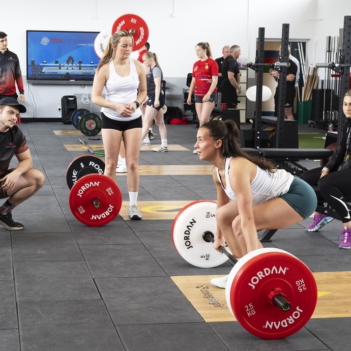 A group of students watching a young woman deadlift