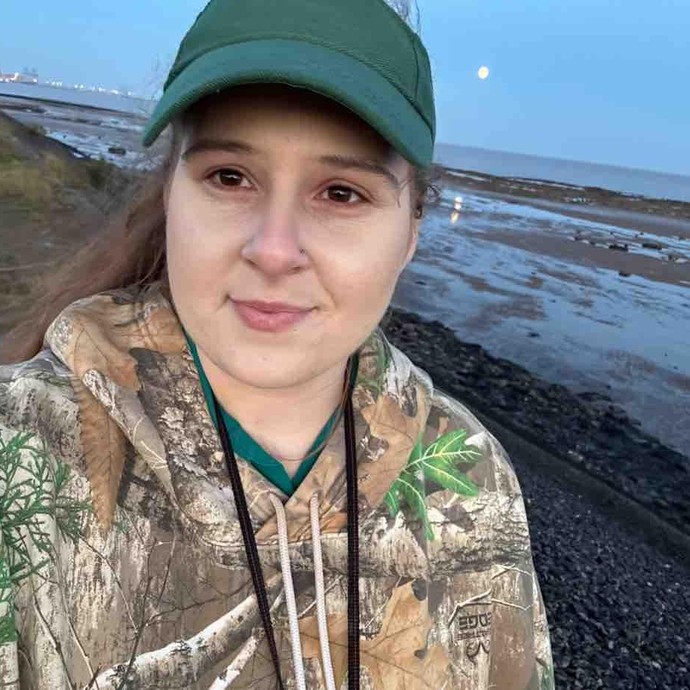 Abbi with a beach behind her wearing a green hat 