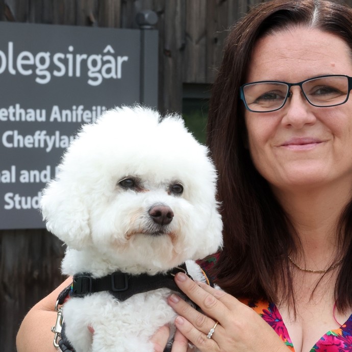 Mandy outside the animal studies centre (with sign) holding her white furred dog Daisy